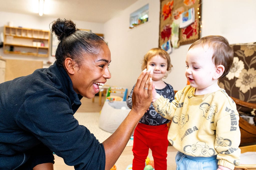 A woman and a child share a joyful high five in a bright nursery setting.