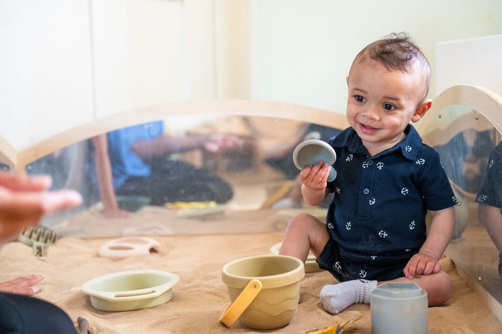 1. A baby boy happily playing in a sand pit, surrounded by toys and sand, enjoying in nursery