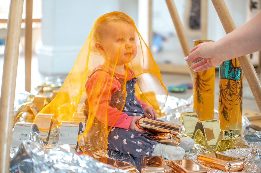 A child happily plays inside a gold and silver play tent in a cozy nursery setting